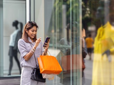 Asian woman using the smart mobile phone for check online shopping order is completed with clothes beside the glassess in store shop with happy action at department center