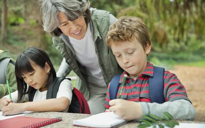 Students making notes at picnic table while adult woman looks on