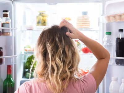 woman standing in front of open fridge, scratching her head