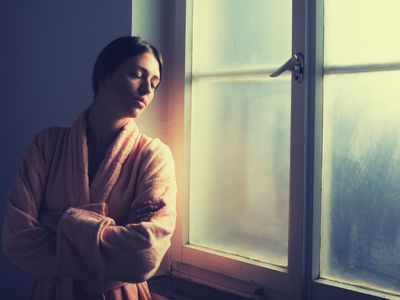 Anxious woman wearing a robe standing alone by the window