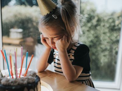 little girl wearing birthday hat look grumpily at her birthday cake