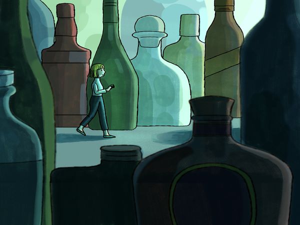 A woman walks among alcohol bottles.