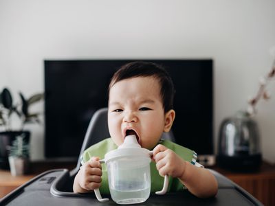 cute baby drinking water from sup cup on high chair