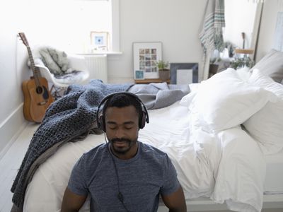 man meditating with headphones on next to his bed