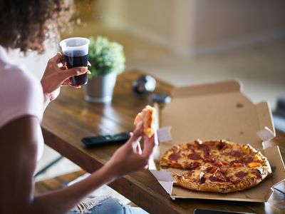woman eating pizza and drinking cola while sitting on sofa