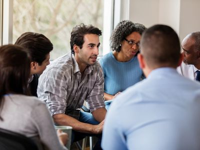 Vulnerable mid adult man talks in group therapy meeting