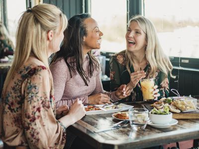 A front view shot of three beautiful mid-adult women enjoying brunch together in a restaurant, they are sitting around a table and laughing with each other.