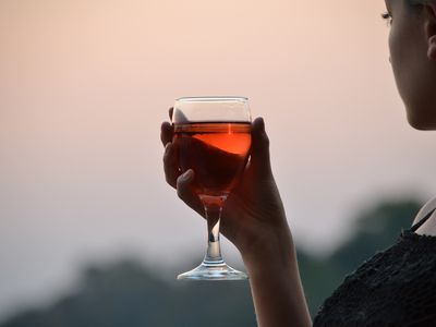 Close-Up Of Woman Holding Wineglass Against Sky During Sunset