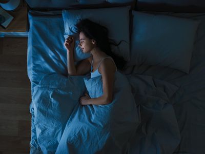 Top View of Young Woman Sleeping Cozily on a Bed in Bedroom at Night