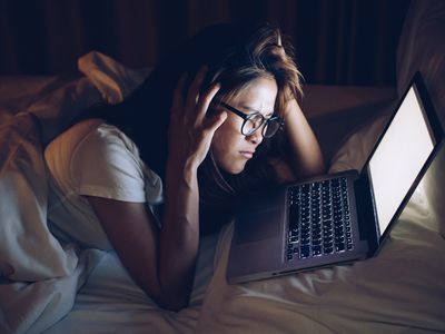 Distressed young woman looking at laptop in bed in the dark
