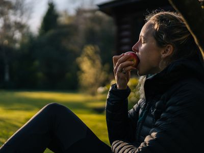 young woman relaxes in garden while eating an apple