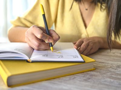 An unrecognizable woman in yellow clothes writes on her datebook