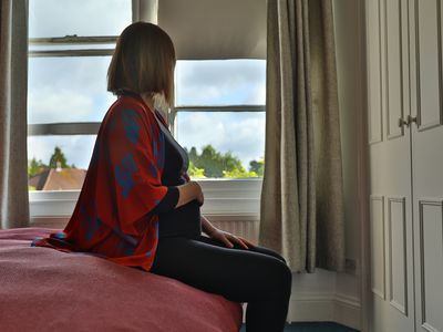 Lone pregnant woman sitting on the bed looking out at the window in the morning