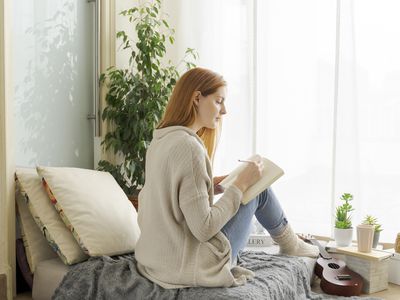 Woman with red hair writing in a journal on the bed.