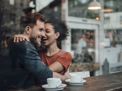 Cheerful woman sitting with arm around on man at cafe