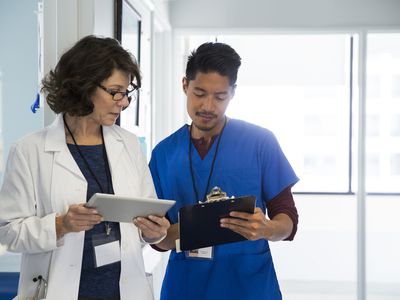 Doctor with male nurse holding digital tablet while discussing in mental hospital corridor 