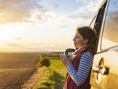 A woman (in her 40s) takes in the view of the countryside from her campervan. She looks contented and relaxed