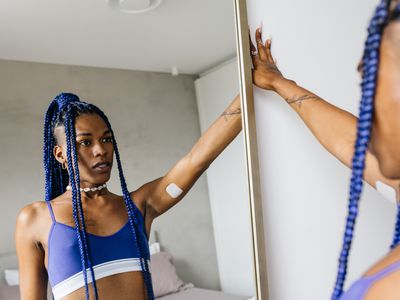 Portrait of a trans woman wearing blue braid looking at herself in bedroom mirror.
