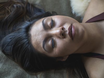 Young woman lying on her back with tear running down her cheek eyes closed