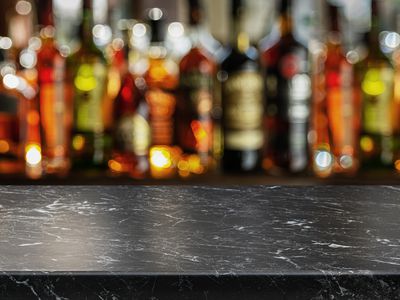 Grey table top and beautiful bokeh shelves with alcohol bottles at the background.