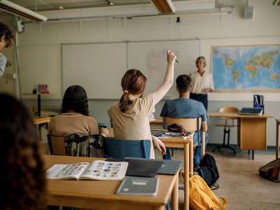 Teenage girl raising hand in high school classroom 