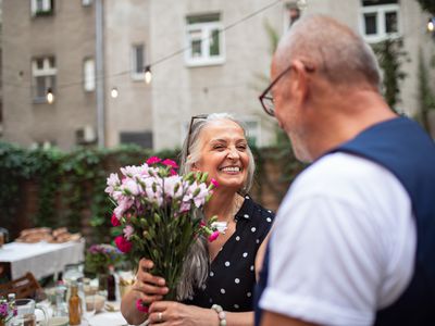 Happy senior woman getting bouquet from her husband outdoors in garden