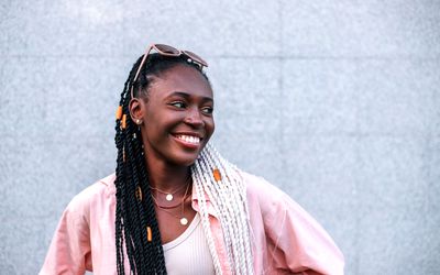 Young black braided woman smiling outdoors in the summer against gray background.