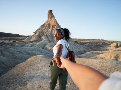 Lovely POV photo of Latin young woman leading her boyfriend into a natural sand castle at desert, looking and smiling to camera.