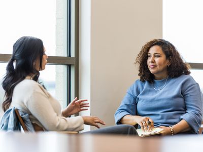 A young adult woman gestures as she shares with her mature adult female counselor.