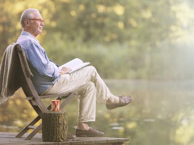 Older man reading book on dock at lake