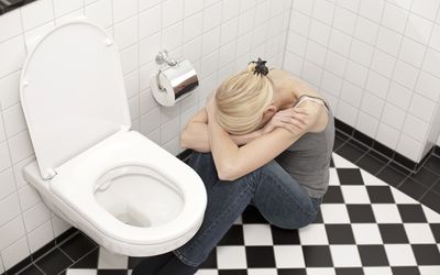 Woman on the floor sits by toilet