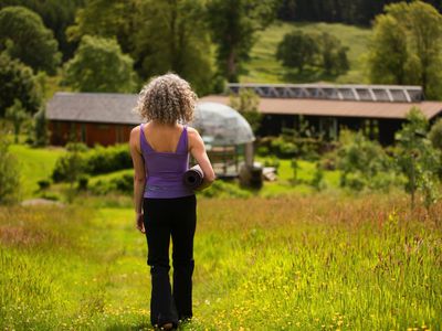 Rear view of mature woman carrying yoga mat walking in eco lodge field