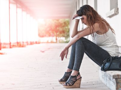 Woman sitting on step with phone in hand looking exhausted or sad
