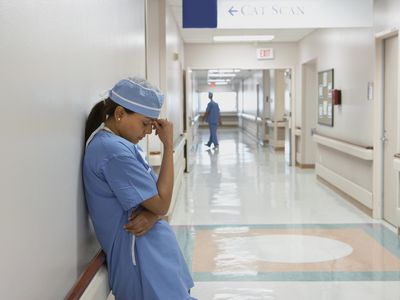 female doctor leaning against wall with head in hand