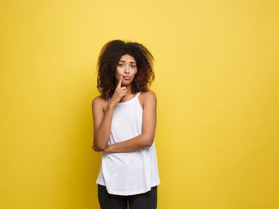 Portrait Of Thoughtful Young Woman Standing Against Yellow Background