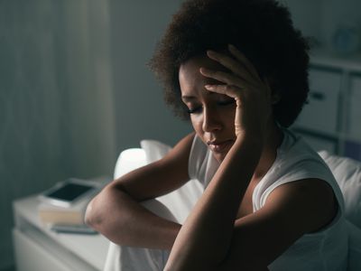 Sad depressed woman suffering from insomnia, she is sitting in bed and touching her forehead, sleep disorder and stress concept