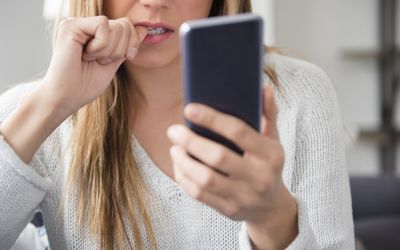 Woman looking at phone while biting nail.