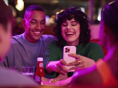 Cheerful woman taking selfie with man on smart phone by friends at bowling alley