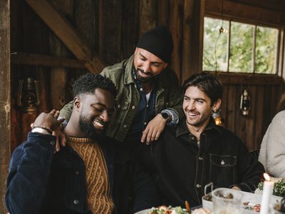 Friends eating together in a barn, one man puts his arm over another man's shoulder.