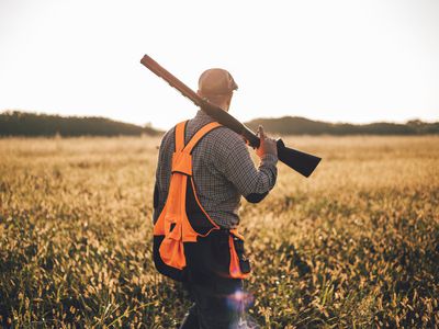 Man walking through a field with a shot gun over his shoulder
