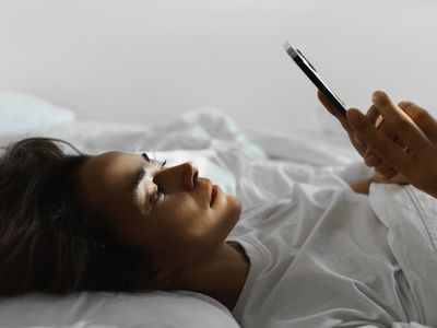 Young woman lying on her back in bed looking at her phone