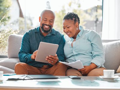 Couple looking at a paper and tablet together in their living room. 