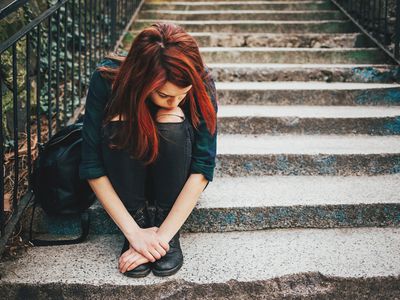 teenage girl with red hair sitting on stone steps looking sad