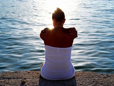 Rear view of young woman sitting by sea