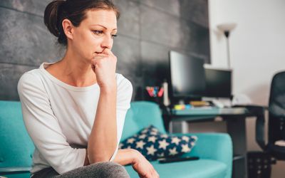 Worried, anxious, middle-aged woman sitting on her couch at home